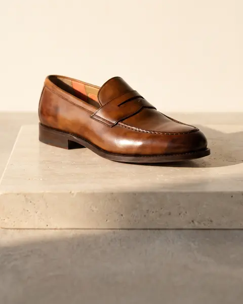 Tan leather penny loafer on a travertine slab in low sun