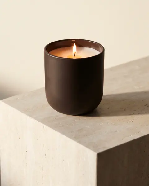 Lit candle in an espresso ceramic vessel on a travertine plinth